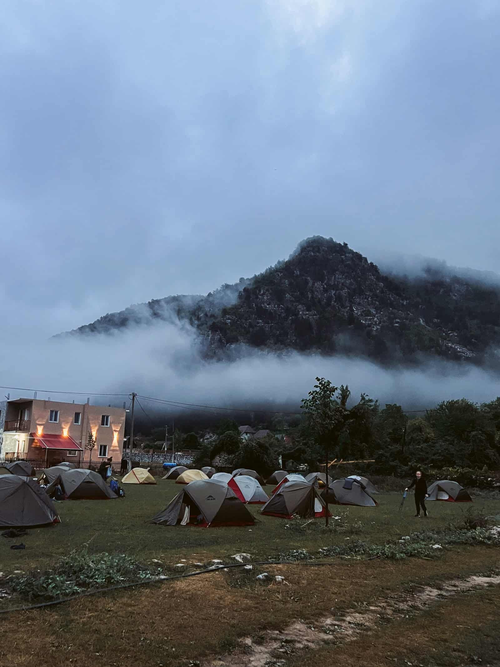 Zeltcamp im Basecamp in Theth am Morgen unter tiefhängenden Wolken, dahinter ein bewaldeter Berg