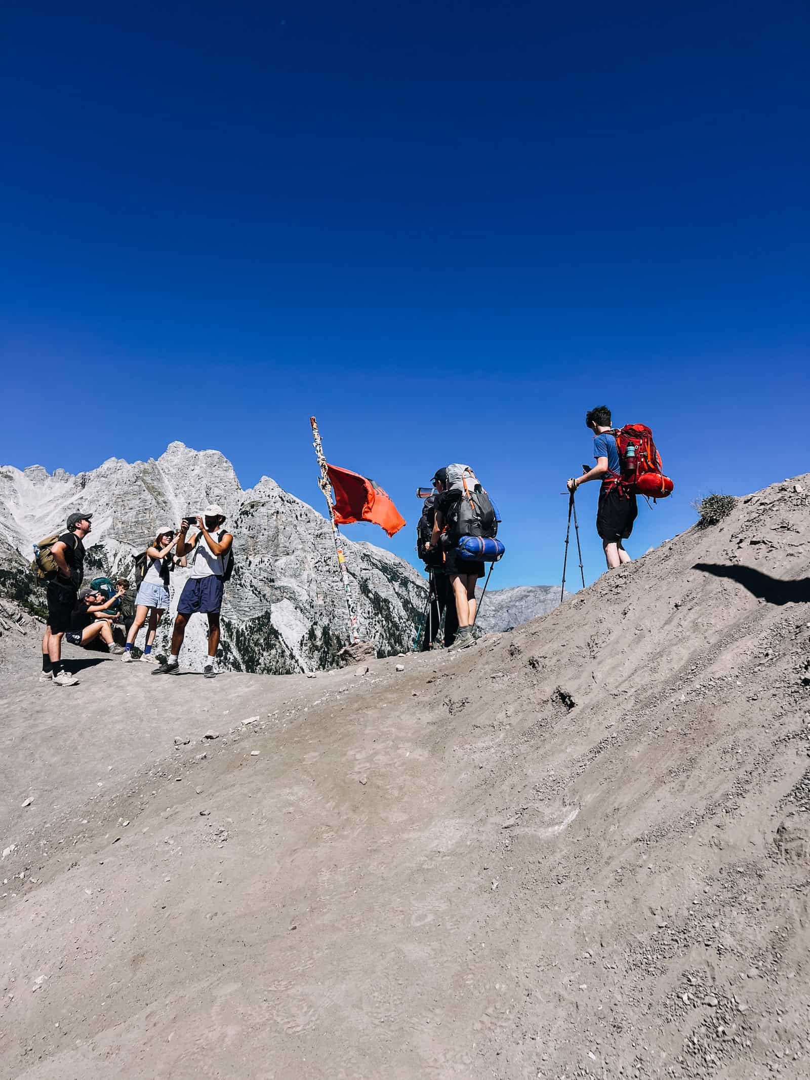 Wanderer am Valbona-Pass mit albanischer Flagge und Felsgipfeln im Hintergrund