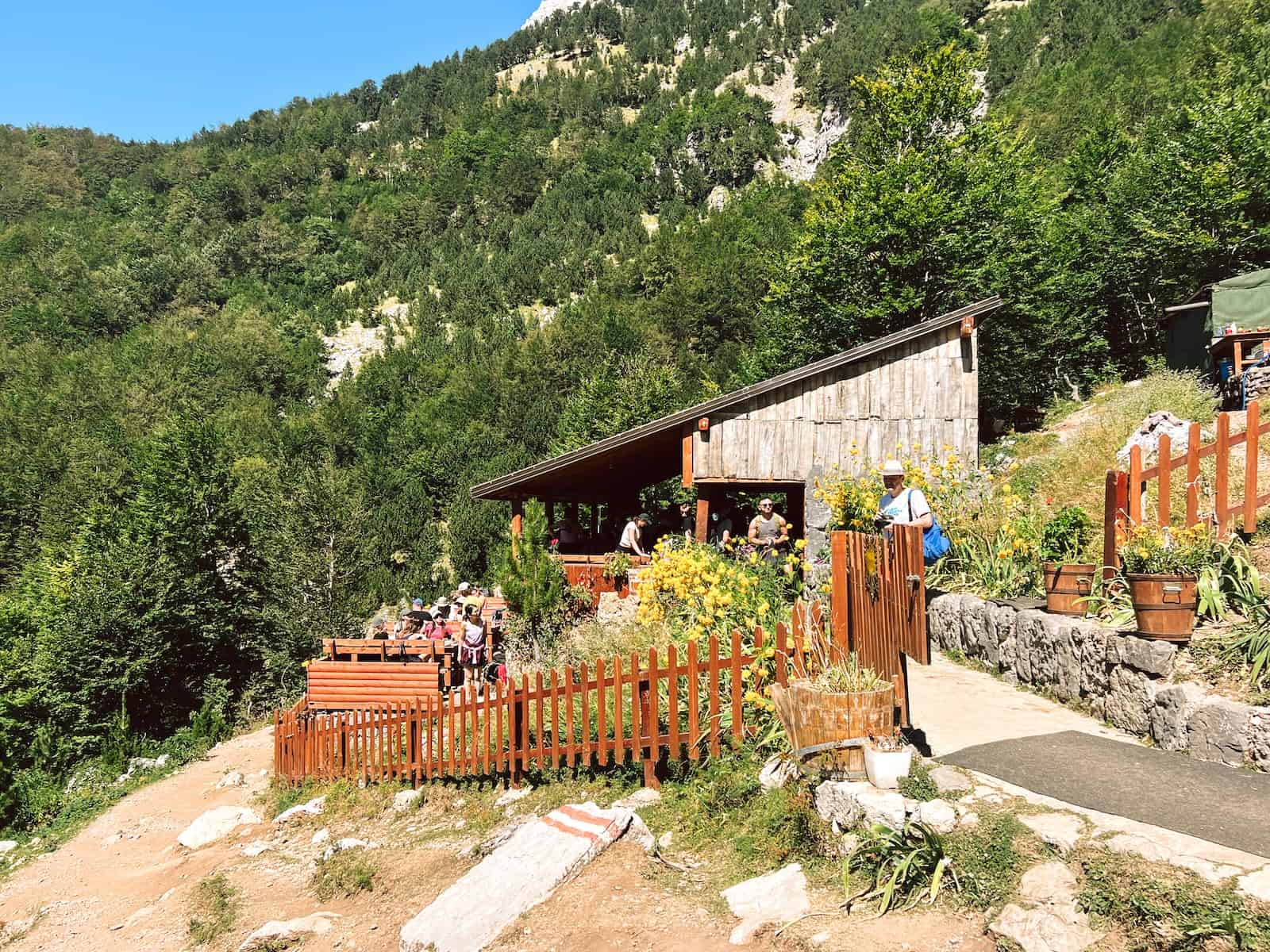 Holzhütte mit Terrasse und Blumen am Hang, Bergbar am Weg auf Etappe 1