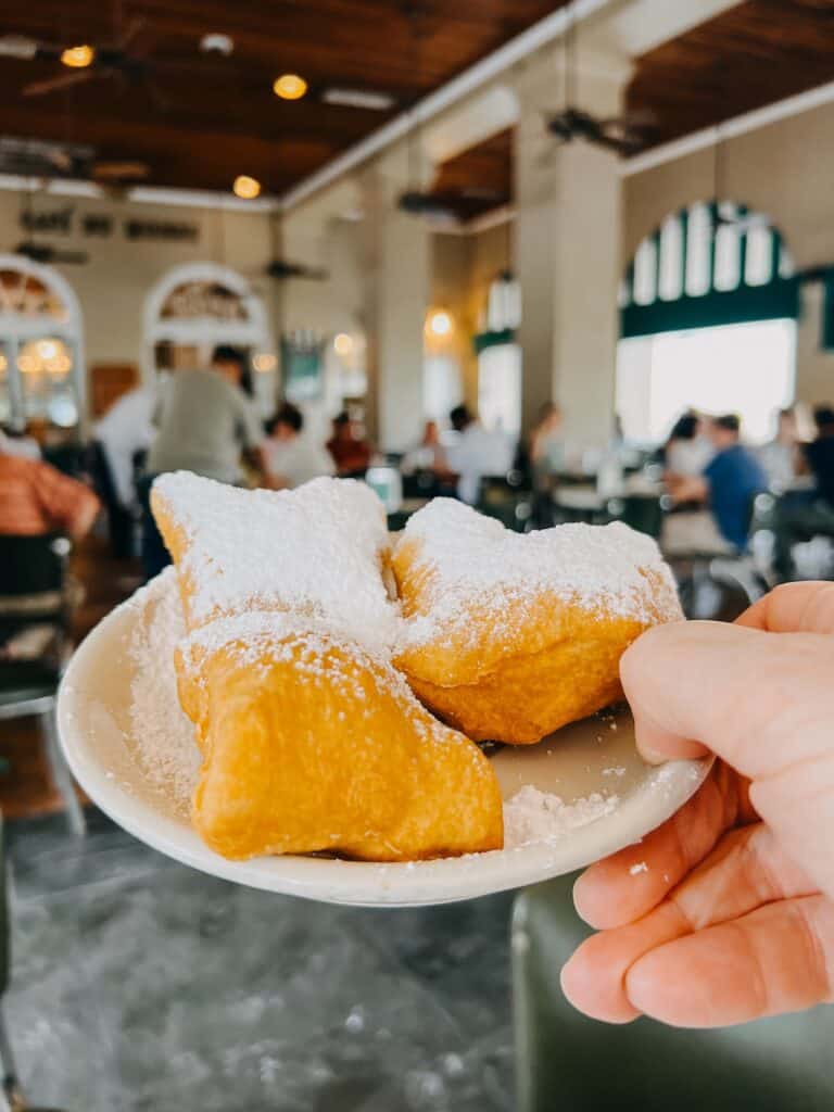 Hand hält einen Teller mit zwei Beignets unter Puderzucker im Café du Monde