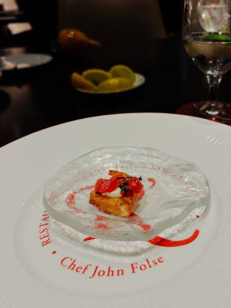 Kleine Vorspeise auf Glasteller mit dem Schriftzug Chef John Folse im Restaurant R'evolution